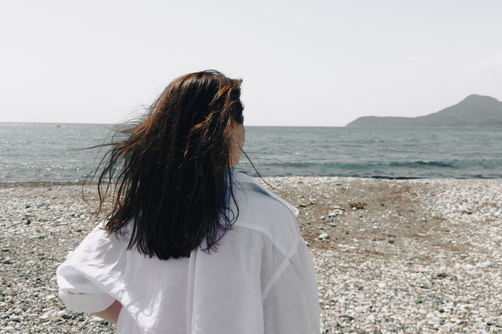 femme-de-dos-qui-admire-la-mer-sur-une-plage-de-galets