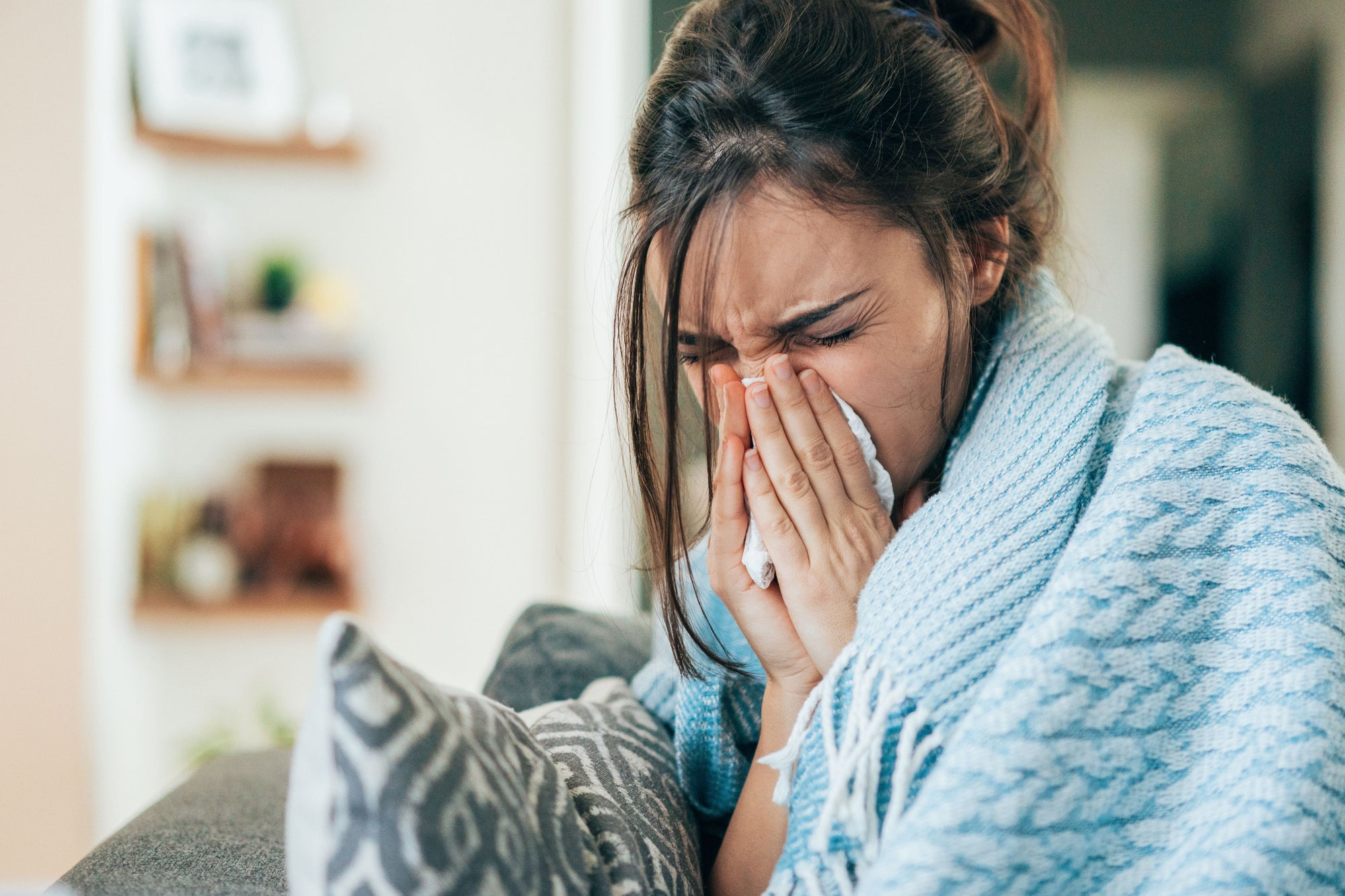 femme-avec-un-plaide-bleu-qui-se-mouche-sur-la-canape-a-cause-de-la-grippe-menstruelle