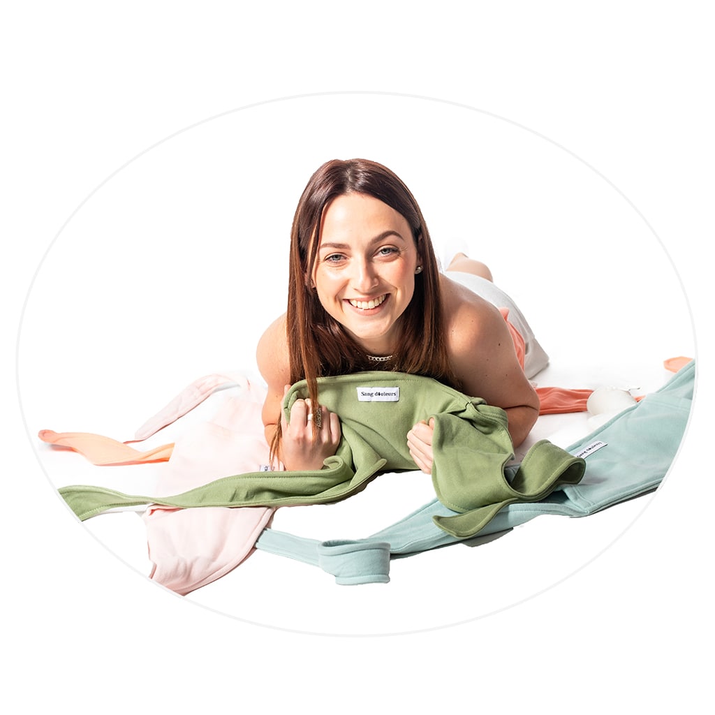 femme-qui-sourit-allongée-au-sol-avec-une-ceinture-bouillotte-verte-entre-les-mains-et-plusieurs-ceintures-sangdouleurs-sur-le-sol